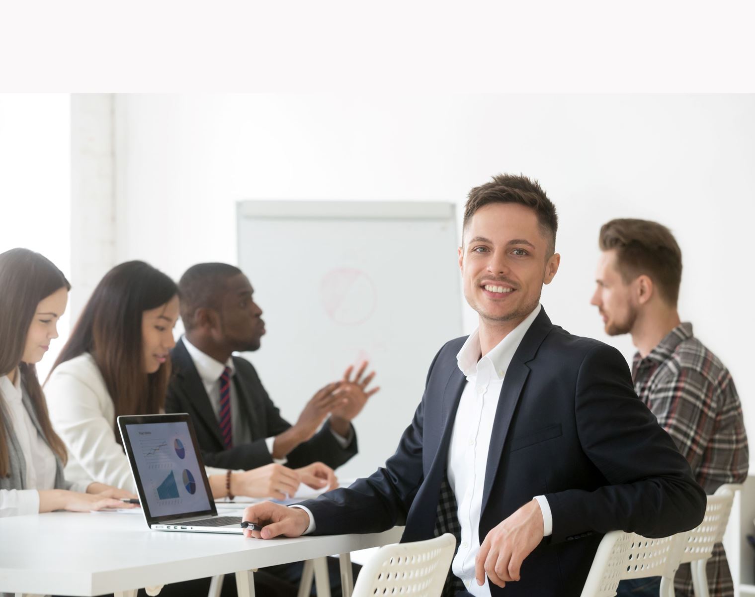 Man sitting at a table looking toward the camera while another group of people are talking in the background